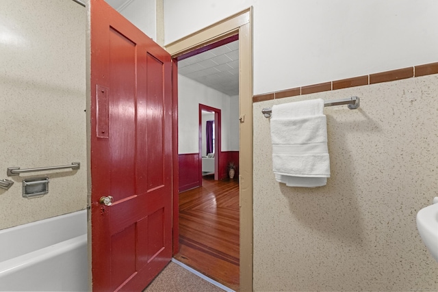 bathroom with a tub to relax in, hardwood / wood-style floors, and tile walls