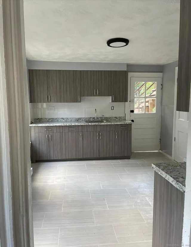 kitchen featuring tasteful backsplash, sink, dark brown cabinets, and light stone countertops