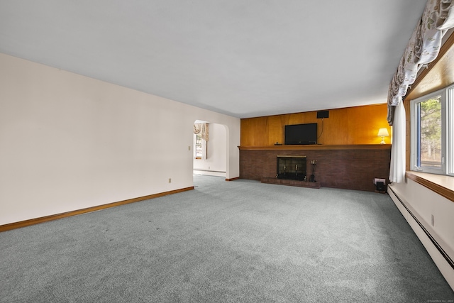 unfurnished living room featuring a brick fireplace, wood walls, carpet floors, and a baseboard radiator