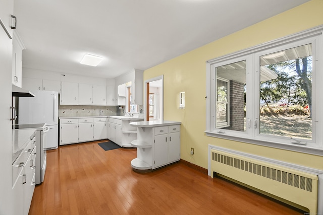 kitchen with radiator, sink, backsplash, wood-type flooring, and white cabinets