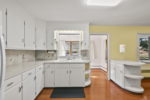 kitchen featuring kitchen peninsula, sink, hardwood / wood-style floors, radiator heating unit, and white cabinetry