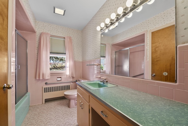 full bathroom with vanity, shower / bath combination with glass door, radiator, toilet, and tile walls