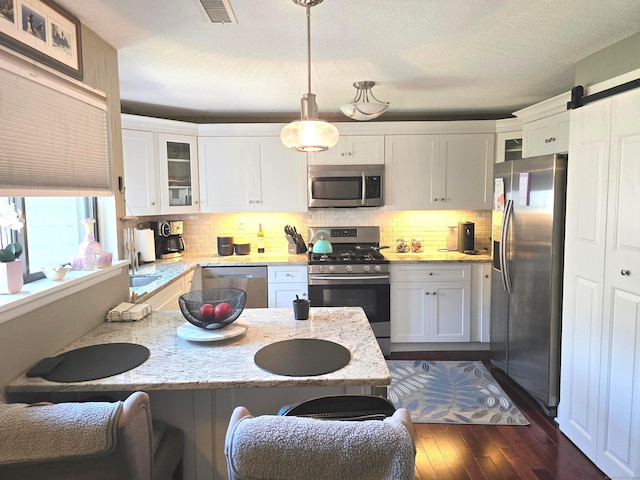 kitchen featuring light stone countertops, stainless steel appliances, white cabinets, dark hardwood / wood-style floors, and hanging light fixtures