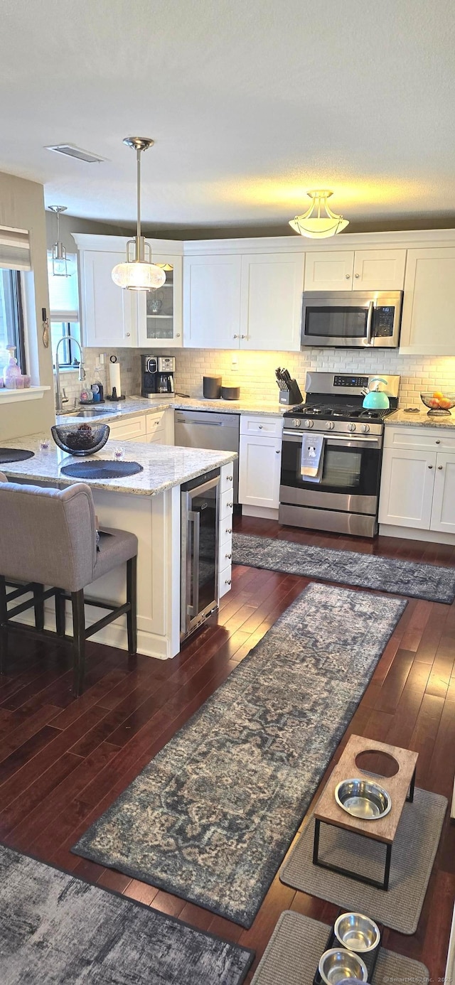 kitchen with sink, white cabinets, beverage cooler, hanging light fixtures, and stainless steel appliances