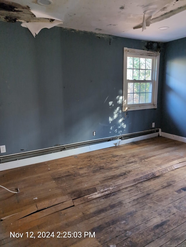 spare room with wood-type flooring, ceiling fan, and a baseboard heating unit