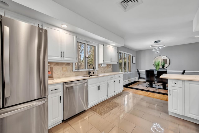 kitchen with appliances with stainless steel finishes, backsplash, sink, light tile patterned floors, and white cabinets