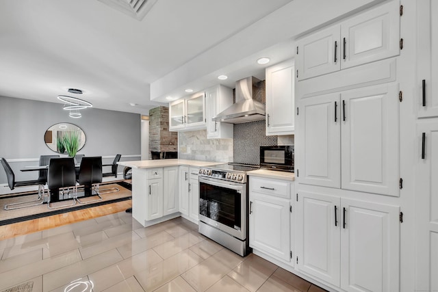 kitchen with stainless steel range with electric stovetop, wall chimney exhaust hood, white cabinetry, and backsplash