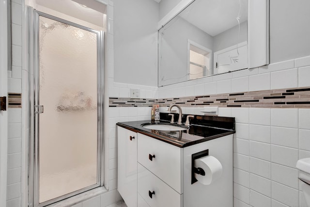 bathroom with backsplash, a shower with door, vanity, and tile walls