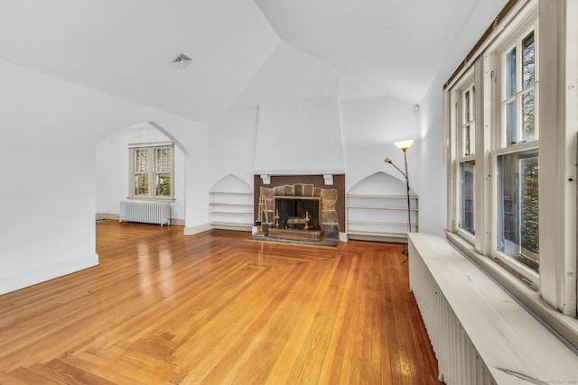 unfurnished living room featuring a fireplace, built in features, vaulted ceiling, and radiator