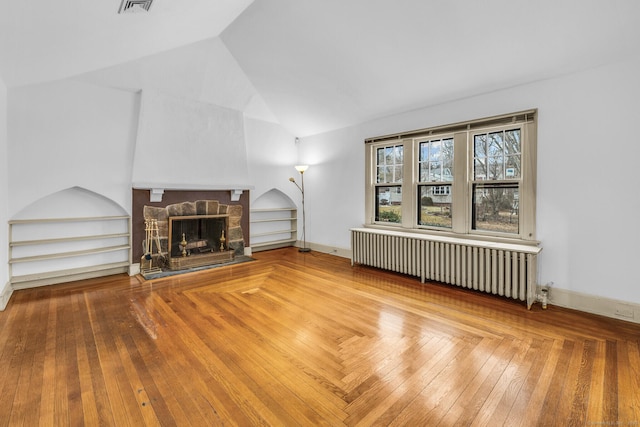 unfurnished living room featuring lofted ceiling, built in features, radiator heating unit, and a stone fireplace