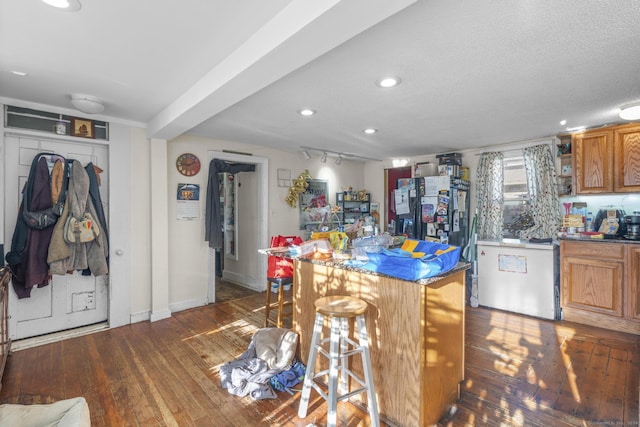 kitchen with dark hardwood / wood-style flooring, beamed ceiling, refrigerator, a textured ceiling, and a breakfast bar