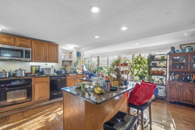 kitchen with a center island, dark hardwood / wood-style floors, dark stone countertops, a textured ceiling, and black appliances