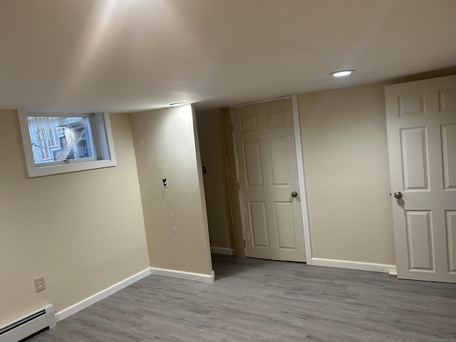 basement with light hardwood / wood-style flooring and a baseboard heating unit