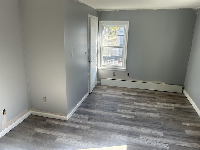 unfurnished room with baseboard heating and dark wood-type flooring