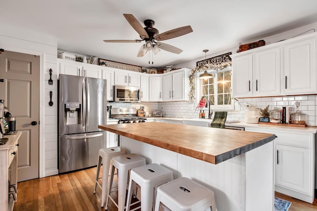 kitchen with wood counters, white cabinets, light wood-type flooring, appliances with stainless steel finishes, and a kitchen island