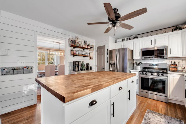 kitchen featuring a center island, wooden counters, wooden walls, appliances with stainless steel finishes, and white cabinetry