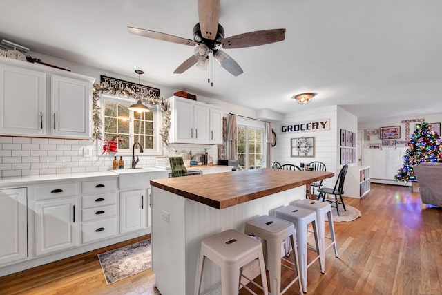 kitchen with light hardwood / wood-style floors, ceiling fan, white cabinets, butcher block countertops, and a kitchen island