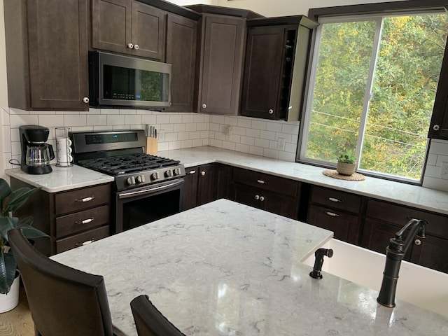 kitchen with stainless steel appliances, light stone countertops, dark brown cabinets, and backsplash