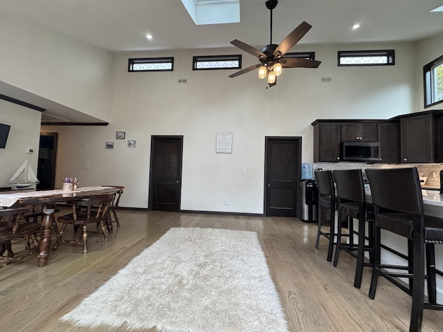 dining space with a towering ceiling, ceiling fan, and light wood-type flooring