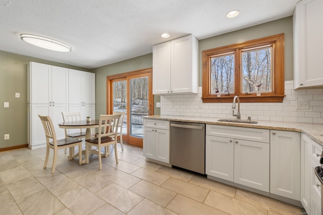 kitchen with sink, white cabinetry, stainless steel dishwasher, light stone countertops, and backsplash