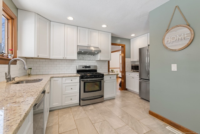 kitchen with sink, backsplash, stainless steel appliances, light stone countertops, and white cabinets