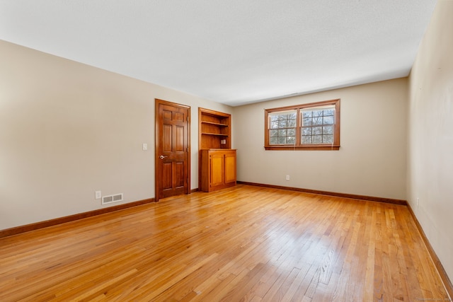 empty room with light hardwood / wood-style floors, built in features, and a textured ceiling