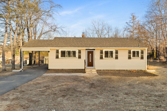 view of front of property featuring a carport, a chimney, driveway, and a shingled roof