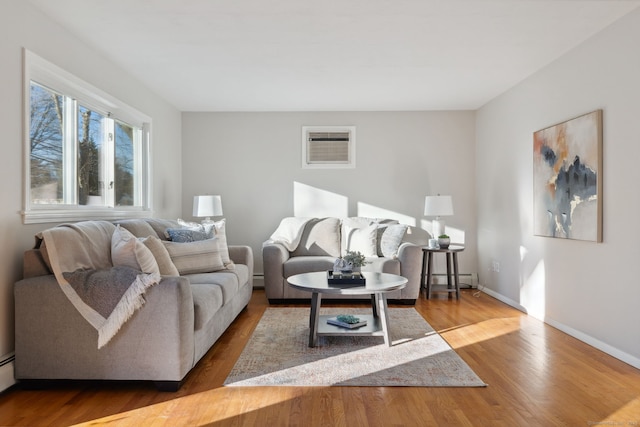 living area with baseboard heating, wood finished floors, baseboards, and a wall mounted air conditioner