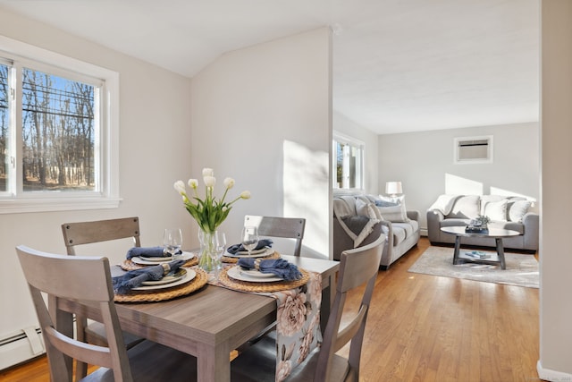 dining room with a baseboard heating unit, vaulted ceiling, light wood-style flooring, and a wall mounted air conditioner