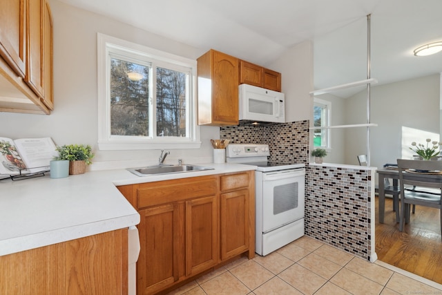 kitchen with a sink, white appliances, a healthy amount of sunlight, and light tile patterned floors