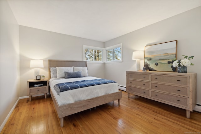 bedroom with a baseboard heating unit, baseboards, and light wood-type flooring