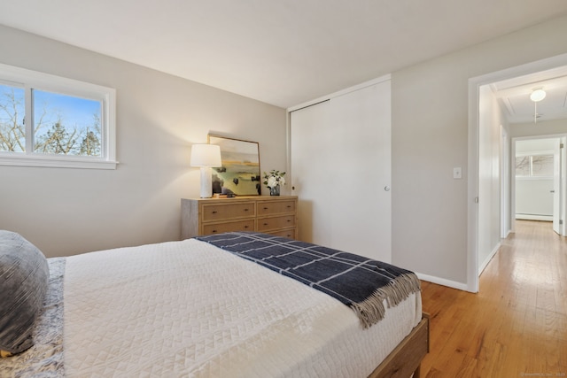 bedroom with baseboards, attic access, light wood-style floors, a closet, and a baseboard radiator