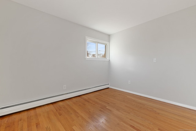 spare room with a baseboard heating unit, wood finished floors, and baseboards