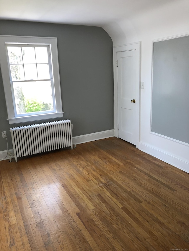 unfurnished room with dark hardwood / wood-style flooring, vaulted ceiling, and radiator