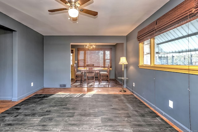 empty room featuring ceiling fan with notable chandelier and dark hardwood / wood-style flooring