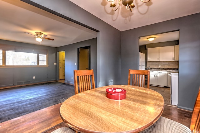 dining room with ceiling fan with notable chandelier and dark wood-type flooring