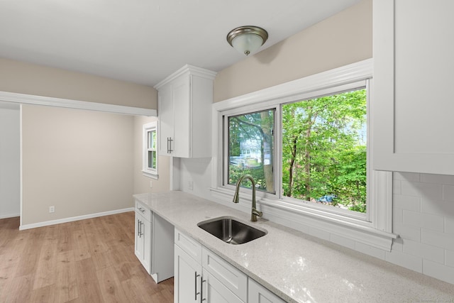 kitchen featuring sink, light hardwood / wood-style flooring, light stone countertops, tasteful backsplash, and white cabinetry