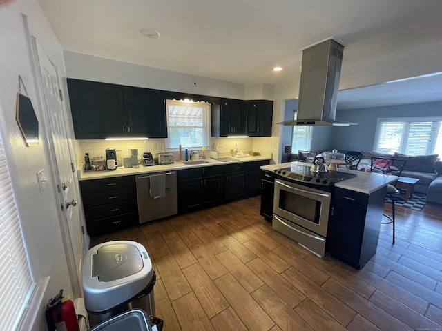 kitchen with island exhaust hood, appliances with stainless steel finishes, decorative backsplash, dark wood-type flooring, and sink