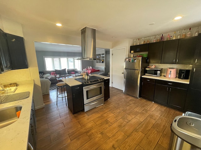 kitchen featuring island exhaust hood, appliances with stainless steel finishes, tasteful backsplash, sink, and light hardwood / wood-style floors