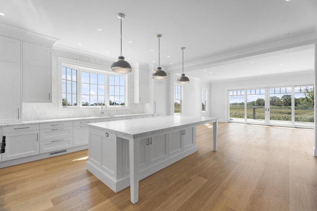 kitchen with backsplash, sink, hanging light fixtures, a kitchen island, and white cabinetry