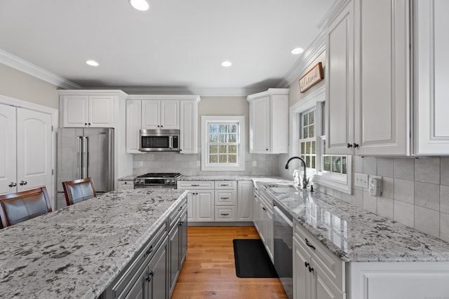 kitchen featuring white cabinets, crown molding, appliances with stainless steel finishes, light hardwood / wood-style floors, and a breakfast bar area