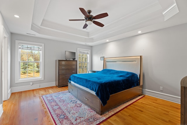 bedroom featuring ceiling fan, a raised ceiling, light hardwood / wood-style flooring, and multiple windows