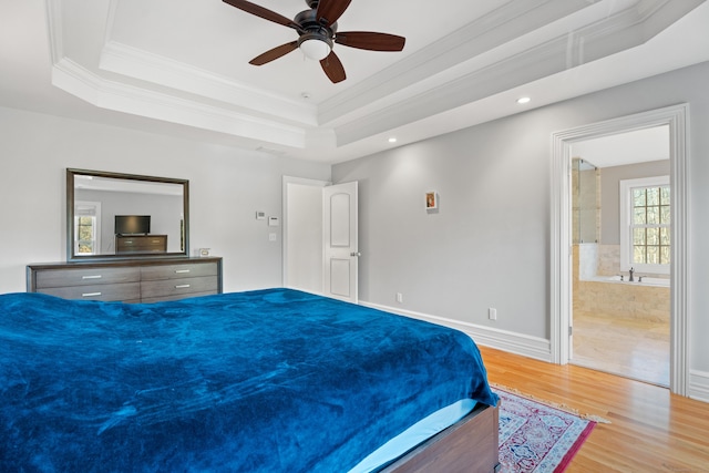 bedroom featuring light wood-type flooring, ensuite bathroom, a raised ceiling, ceiling fan, and crown molding