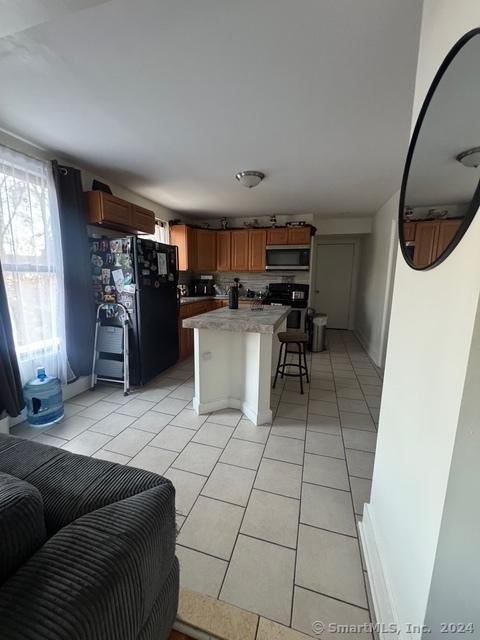 kitchen with a kitchen bar, light tile patterned floors, black appliances, and a kitchen island