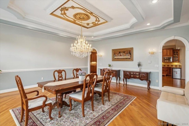 dining room with a tray ceiling, light hardwood / wood-style flooring, ornamental molding, and a chandelier