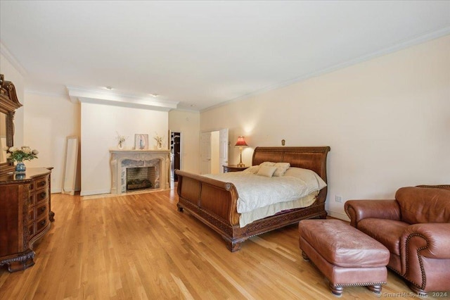 bedroom featuring a fireplace, ornamental molding, and light wood-type flooring