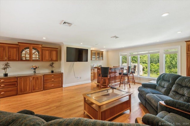 living room with crown molding, bar area, and light hardwood / wood-style floors