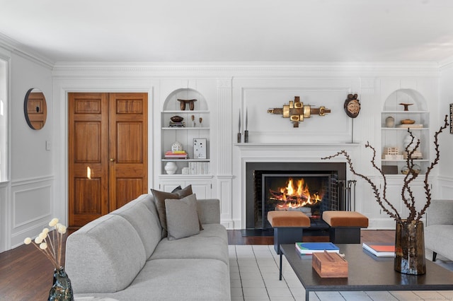 living area featuring built in features, crown molding, a decorative wall, a premium fireplace, and wood finished floors