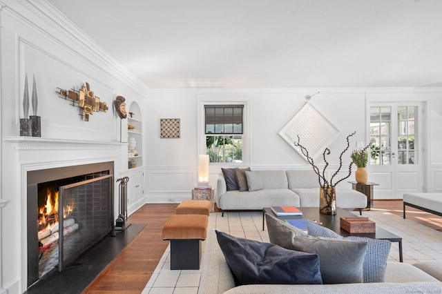 living room with built in shelves, crown molding, a decorative wall, a fireplace with flush hearth, and tile patterned flooring