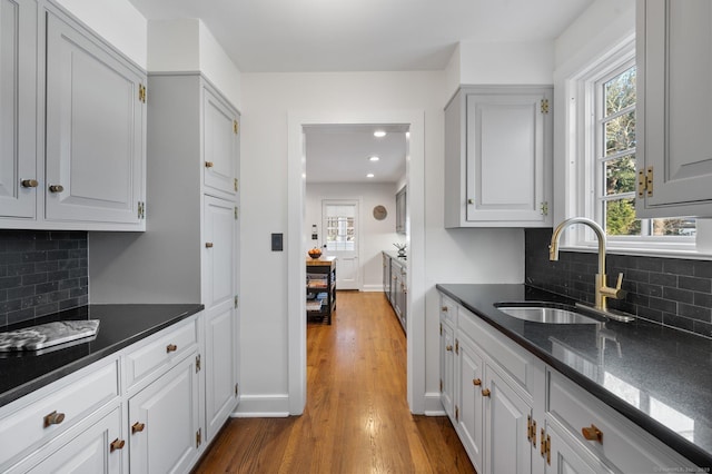 kitchen with wood finished floors, a sink, baseboards, tasteful backsplash, and dark stone countertops